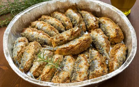 Sardine al forno dorate e croccanti, disposte in una teglia d'alluminio con rametti di rosmarino.