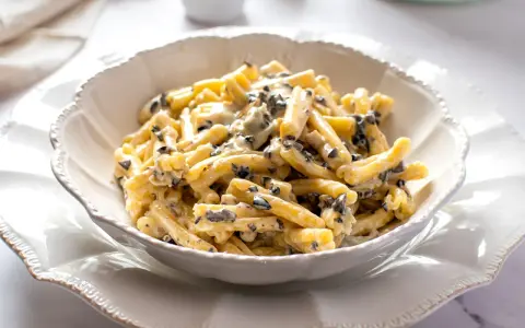 Un piatto di pasta alla cenere cremosa, con pezzetti scuri di olive, servita in una ciotola bianca decorata.