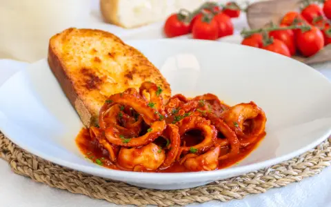 Un piatto invitante di moscardini in umido, con tentacoli succulenti in salsa rossa, accompagnati da una fetta di pane tostato dorato.