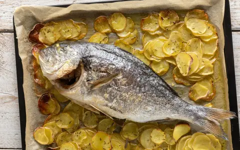 Orata al forno dorata e succulenta, adagiata su un letto di patate croccanti e aromatiche.
