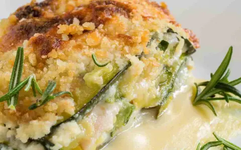 Una fetta di parmigiana di zucchine bianca senza besciamella, dorata e croccante, con rosmarino fresco.