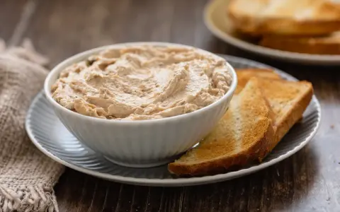 Una ciotola di cremosa mousse di tonno, servita con fette di pane tostato dorato. Perfetta per un aperitivo veloce.