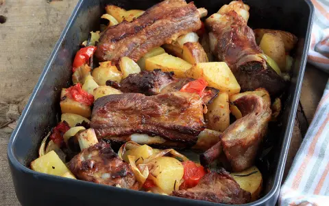 Succulente costine al forno con patate, peperoni e cipolle in una teglia.