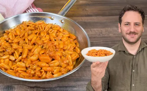 Un uomo sorride mostrando una ciotola di gnocchetti alla campidanese, accanto a una padella piena dello stesso piatto.