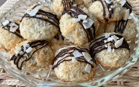 Deliziosi dolcetti al cocco, ricoperti da cioccolato fondente e scaglie di cocco croccante, su un piatto di vetro.
