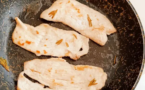 Tre fette di tacchino in padella, morbido e profumato al rosmarino, pronte per essere gustate.