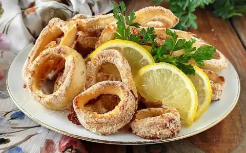 Anelli di calamari al forno dorati e croccanti, guarniti con spicchi di limone fresco e prezzemolo.