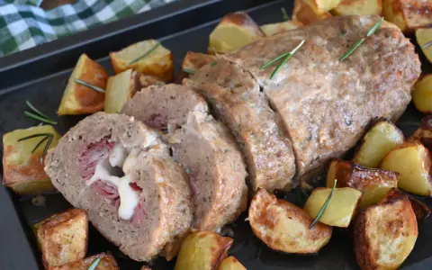 Polpettone al forno ripieno di prosciutto e formaggio filante, servito con patate arrosto e rosmarino.