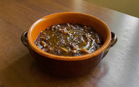 Un gustoso piatto di pasta e lenticchie, condito con olio d'oliva, servito in una ciotola di terracotta su un tavolo di legno.