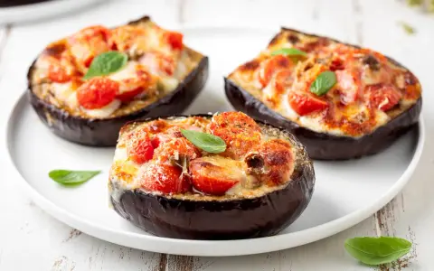 Melanzane ripiene al forno velocissime, con pomodorini, formaggio filante e basilico fresco. Un piatto invitante e facile da preparare.