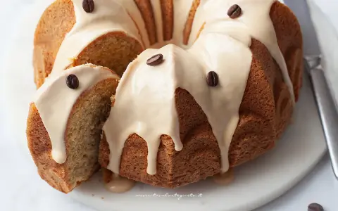Torta al caffè soffice e profumata, ricoperta da una glassa chiara e decorata con chicchi di caffè. Una fetta è stata tagliata, rivelando l'interno morbido.