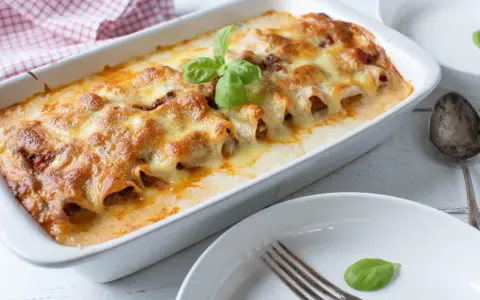 Cannelloni ripieni di carne macinata e mozzarella, cotti al forno e gratinati, con una foglia di basilico fresco.