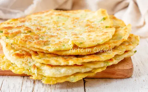 Una pila di schiacciate di zucchine dorate e soffici, cosparse di parmigiano, pronte per essere gustate.