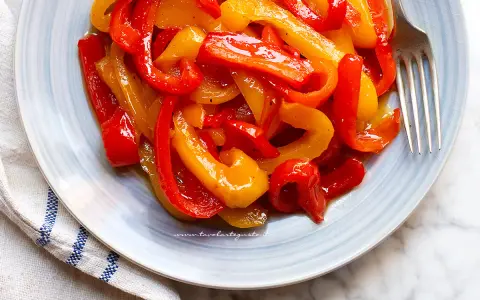 Piatto di peperoni in agrodolce, rossi e gialli, conditi con olio e spezie, pronti per essere gustati.