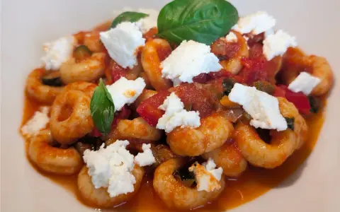 Anellini alla pecorara con pomodoro, zucchine e ricotta fresca, guarniti con foglie di basilico.