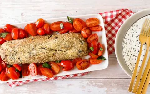 Polpettone di melanzane dorato e croccante, circondato da pomodorini freschi e basilico, pronto per essere gustato.