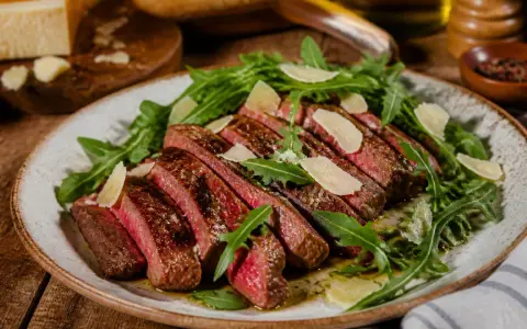 Tagliata di manzo succulenta, affettata e servita su un letto di rucola fresca, guarnita con scaglie di parmigiano.