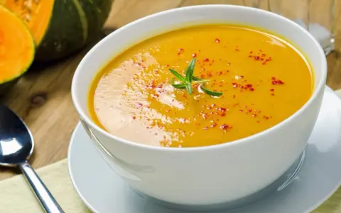 Una cremosa vellutata di zucca, guarnita con rosmarino e paprika, pronta per essere gustata.