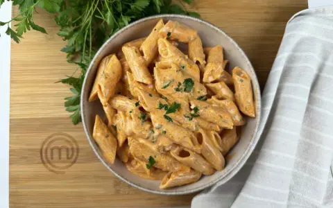 Penne alla vodka cremose e invitanti, guarnite con prezzemolo fresco, su un tagliere di legno con il logo di MasterChef.