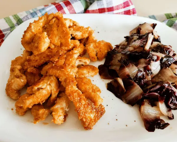 Straccetti di pollo al forno dorati e croccanti, serviti con radicchio stufato. Un piatto semplice e gustoso.