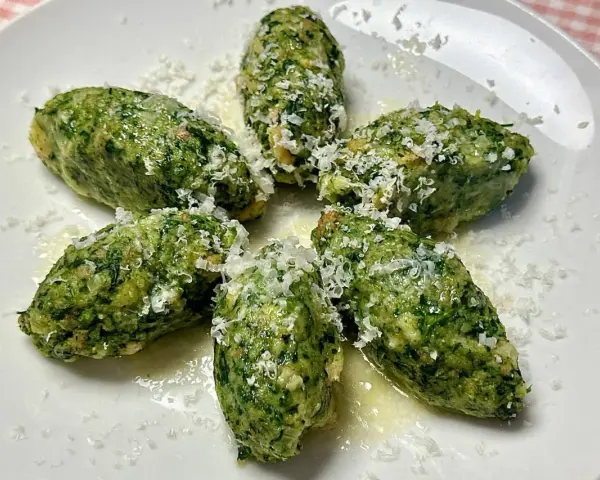 Strangolapreti alla trentina, verdi e saporiti, spolverati di formaggio grattugiato su un piatto bianco.