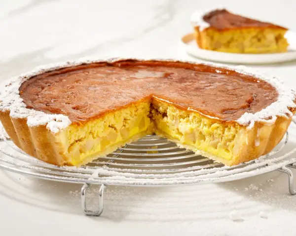 Una fetta di torta di mele con crema pasticcera, cosparsa di zucchero a velo, su una griglia.