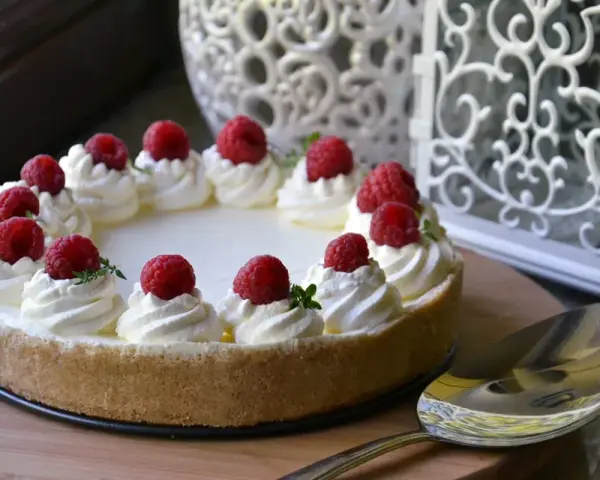 Cheesecake senza gelatina decorata con panna montata e lamponi freschi, pronta per essere servita.