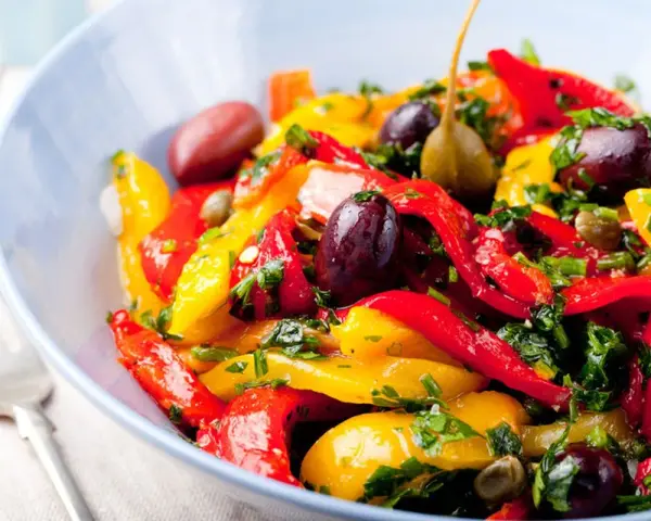 Peperonata ricetta della nonna: un piatto colorato con peperoni rossi e gialli, olive, capperi e prezzemolo fresco.