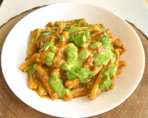 Un piatto di pasta alla Portofino, con un sugo rosso e un pesto verde brillante, guarnito con foglie di basilico fresco.