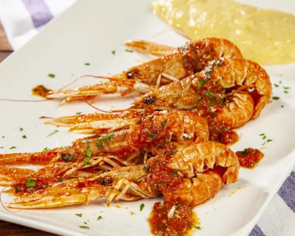 Scampi alla busara succulenti su piatto bianco, con un contorno di polenta gialla.
