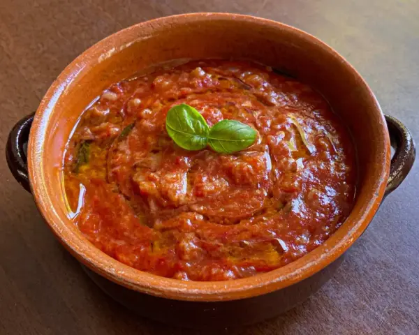 Piatto di pappa al pomodoro in terracotta, guarnito con basilico fresco. Un classico della cucina toscana.