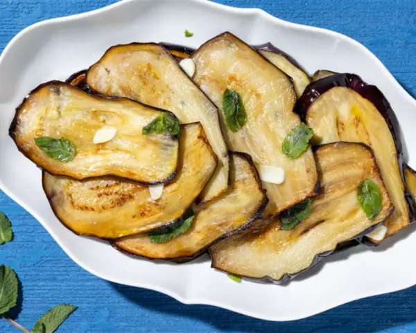 Fette di melanzane grigliate, guarnite con menta fresca e aglio, un contorno di verdure saporito.