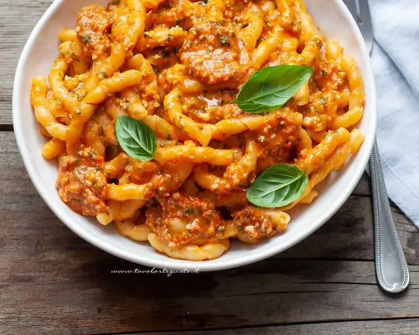 Busiate alla trapanese, un piatto di pasta siciliana con un ricco sugo rosso, guarnito con basilico fresco.