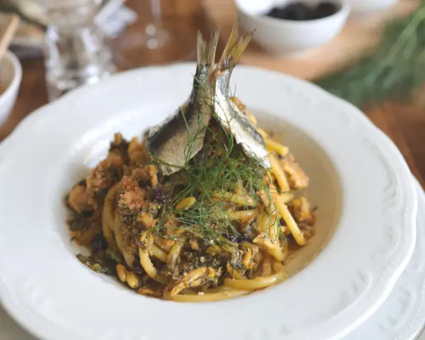 Un piatto di pasta con le sarde, guarnito con finocchietto fresco e due pesciolini interi. Un classico siciliano pronto da gustare.