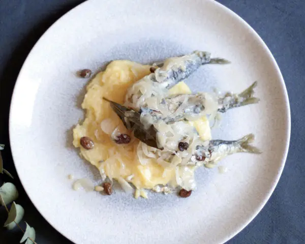 Sarde in saor su un letto di polenta, con cipolle caramellate e uvetta. Un classico veneto.