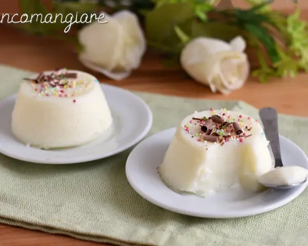 Biancomangiare ricetta originale siciliana: due dolci al cucchiaio bianchi, guarniti con codette colorate e scaglie di cioccolato, su piattini bianchi.