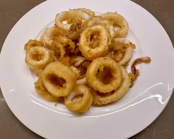 Un piatto bianco pieno di frittura di calamari dorata e croccante, un antipasto invitante.
