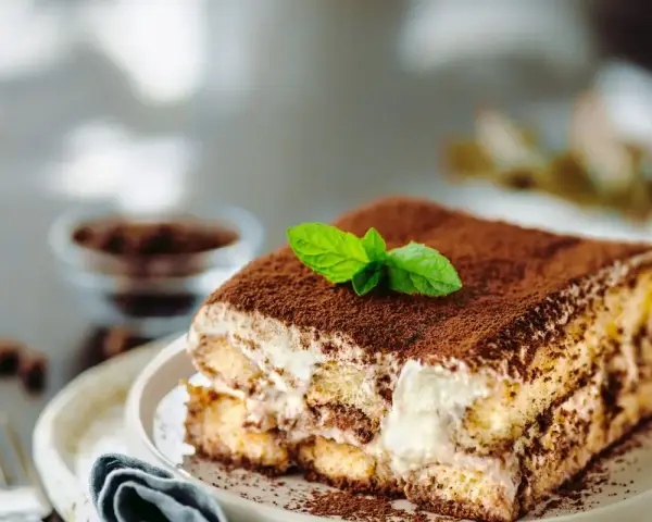 Una fetta di tiramisù ricetta originale, cosparso di cacao e decorato con menta fresca.