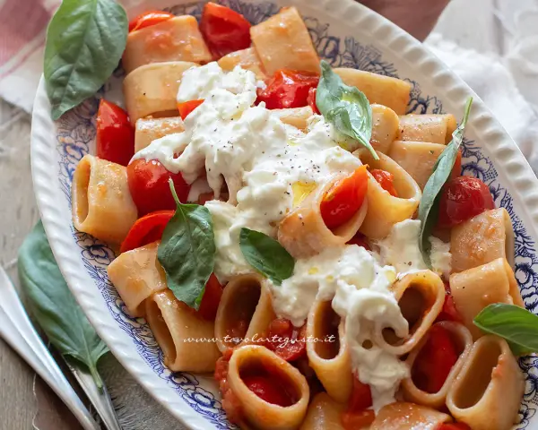 Piatto di pasta con pomodorini e abbondante stracciatella cremosa, guarnito con basilico fresco.