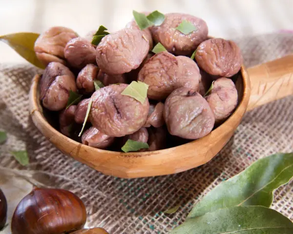 Un cucchiaio di legno trabocca di castagne bollite con buccia, guarnite con foglie verdi. Un assaggio autunnale.