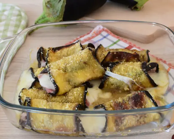 Involtini di melanzane alla siciliana appena sfornati, filanti e dorati, in una pirofila di vetro.