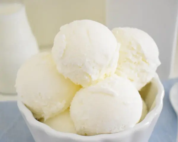Coppa di gelato cremoso, risultato di una perfetta ricetta gelato con gelatiera. Latte fresco e cucchiaino bianco.