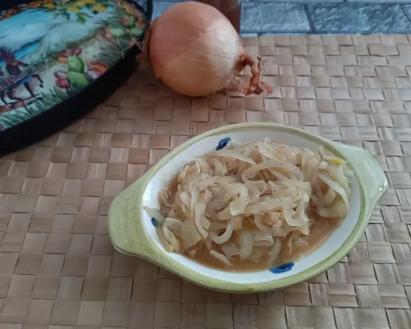 Ciotola con cipolle in agrodolce, accanto una cipolla intera e un piatto decorato.