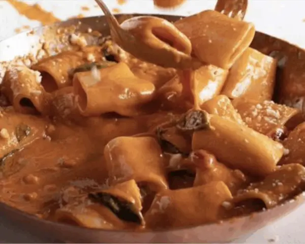 Un primo piatto cremoso e invitante: paccheri alla Vittorio, conditi con una ricca salsa arancione e guarniti con parmigiano.