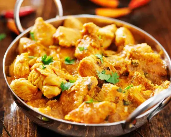 Bocconcini di pollo al curry, un piatto speziato e profumato, servito in una ciotola metallica su un tavolo di legno.