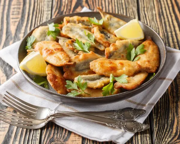 Piatto di acciughe ripiene alla ligure, dorate e croccanti, guarnite con prezzemolo fresco e spicchi di limone.