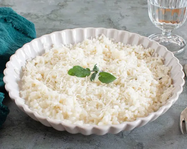 Piatto di riso in cagnone, cremoso e invitante, guarnito con foglie di salvia e parmigiano grattugiato.
