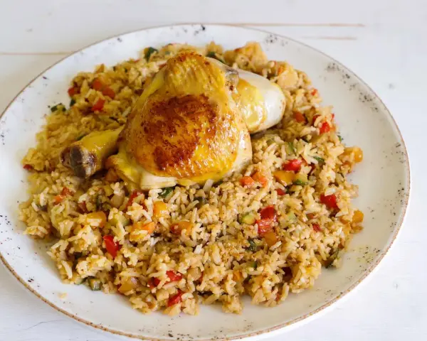 Fusi di pollo in padella serviti su un letto di riso saltato con verdure colorate.