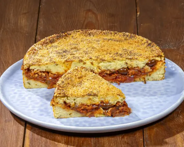 Pitta di patate ripiena di sugo, olive e cipolle, con una crosta dorata di pangrattato.