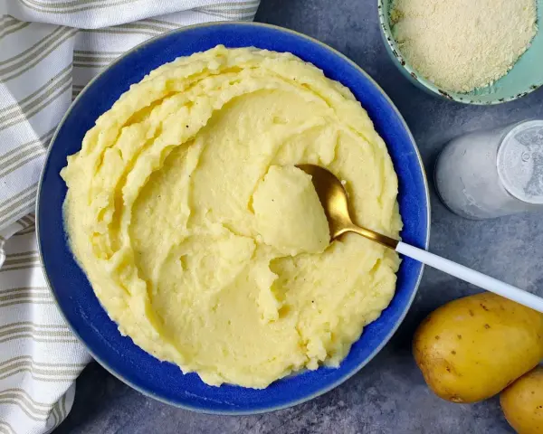 Un piatto invitante di puro di patate cremoso, pronto per essere gustato. Accanto, patate fresche, sale e formaggio grattugiato.